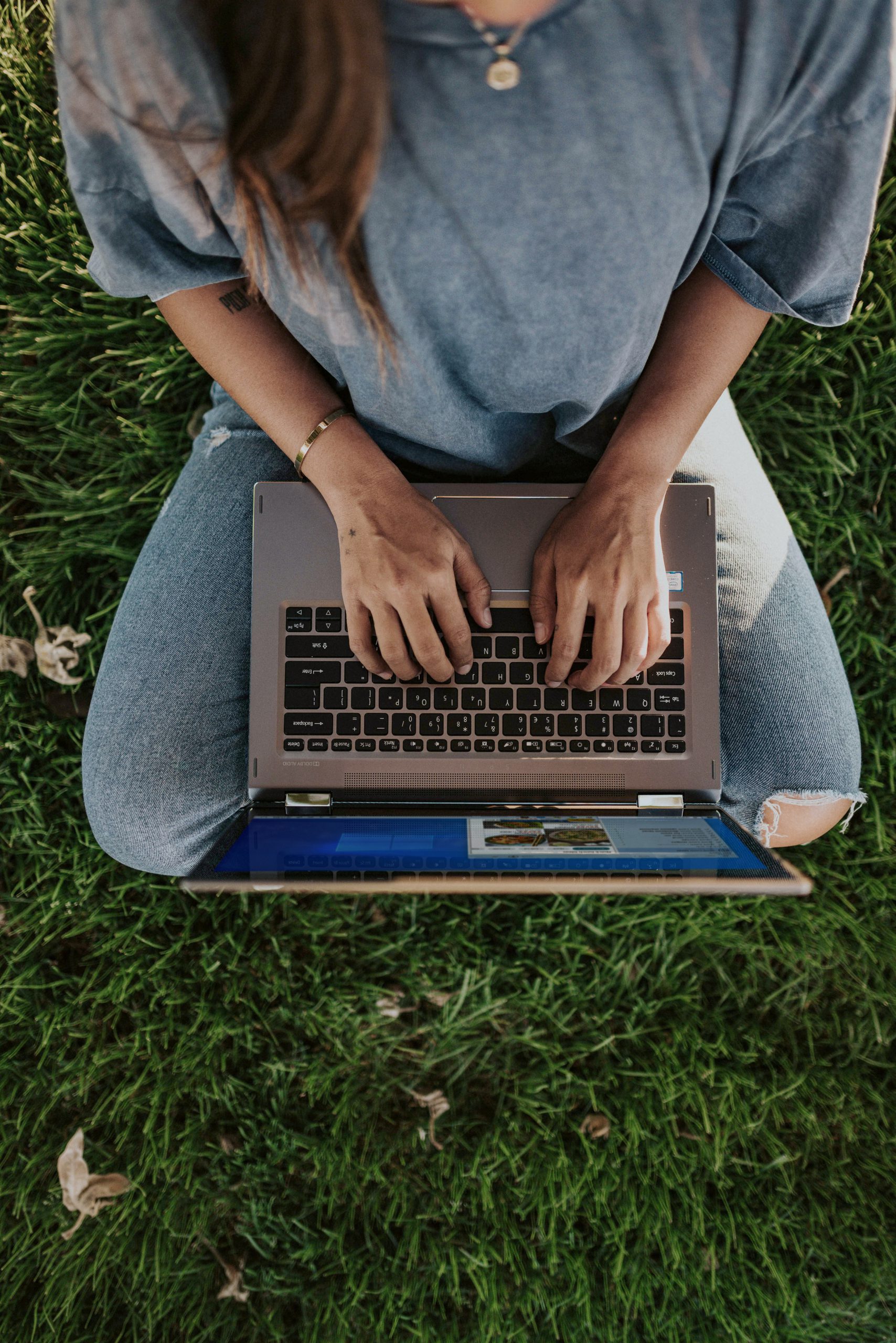 person in blue shirt and blue denim jeans sitting on green grass field using macbook pro